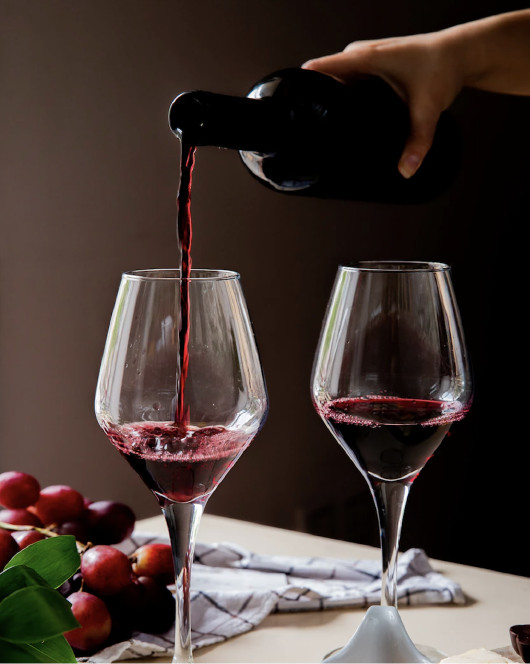Image of a bottle serving two glasses of red wine, fresh grapes and a linen tablecloth